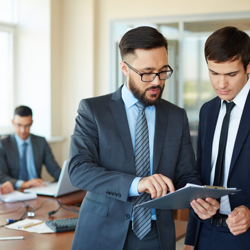 Paperwork Confident businessman pointing at document while explaining his idea to his partner on background of their colleagues